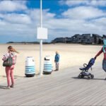 Family Stroll on a Peaceful Beach Boardwalk Family enjoying peaceful beach boardwalk with sand, ocean view, modern houses, and stroller.