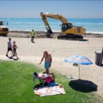 Summer Beach Day With Construction and Relaxation Beach construction site with families relaxing by the ocean on a sunny summer day.