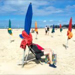 Relaxing Summer Day on a Vibrant Beach Sunny beach day with umbrellas, volleyball, and people relaxing by the ocean.