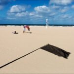 Peaceful Beach Day With Golden Sand and Blue Sky Sunny beach with golden sand, blue sky, lifeguard stands, and people relaxing by the shore.