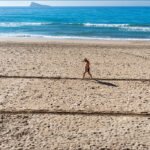 Man Walking on Beach Inside Square in Sand Man walking on beach inside square outline in sand by ocean waves.