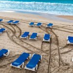 Relaxing Blue Lounge Chairs on Sunny Beachfront Blue lounge chairs on sandy beach by turquoise ocean waves under clear sky.