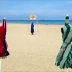 Tranquil Beach Day With Umbrellas and Ocean View Peaceful sandy beach with umbrellas, woman walking, ocean waves, and clear blue sky.