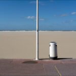 Tranquil Beach Scene With Ocean Waves and Blue Sky Peaceful beach with ocean waves, blue sky, sandy shore, streetlight, and trash bin.