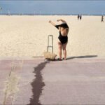 Woman in Black Swimsuit Enjoying Sunny Beach Day Woman in black swimsuit relaxing on sandy beach with ocean view and summer sunshine.