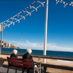Elderly Women Sharing a Peaceful Seaside Moment Elderly women sitting on a beachfront bench enjoying ocean view and peaceful seaside conversation.