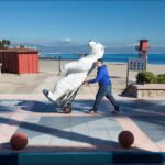 Boy Pushing Polar Bear Statue by the Beach Boy pulling polar bear statue on seaside promenade with beach and mountains.
