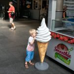 Child Pretends to Lick Giant Ice Cream Cone Indoors Child licking giant plastic ice cream cone at smoothie stand indoors.