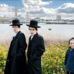 Jewish Boys by River With City Skyline Backdrop Jewish boys standing by river with city skyline and greenery in background.