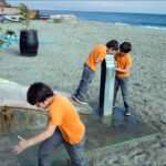 Boys in Orange Shirts Playing by Beach Fountain Boys in orange shirts playing at beach fountain near ocean and boats.