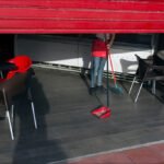 Morning Café Worker Sweeping Floor in Sunlight Cafe worker sweeping floor in morning light with red chairs and wooden tables.