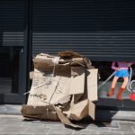 Discarded Cardboard and Cartoon Character in Urban Street Scene Discarded cardboard box outside shuttered storefront with cartoon vacuum cleaner character in window.