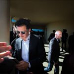 Celebrity in Black Suit Reading Tablet at Fan Event Celebrity in black suit reading tablet while fans crowd for autographs at outdoor event.
