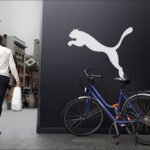 Man Walking by Puma Storefront With Bicycle in City Man walking past Puma storefront with parked bicycle in urban city street scene.