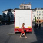Woman in Red Dress Walking Past City Truck Woman in red dress walking past red truck in lively urban city square.