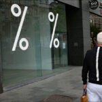 Man Walking Past Storefront With Sale Signs Man walking past city store with sale signs and urban shopping street background.