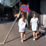 Urban Walk with Friends and Quirky No Parking Sign Two young women walking city street with mural, no parking sign, and urban buildings.