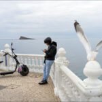 Seaside Promenade With Scooter, Seagull and Ocean View Coastal promenade with electric scooter, people enjoying ocean view, and seagull in flight.