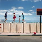 Family Stroll Along Vibrant Seaside Promenade Coastal promenade with people walking by seawall, ocean view, and family enjoying beach day.