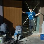 Workers Renovating Storefront with Tools and Debris Construction workers renovating storefront with tools, debris, and taped wooden door.