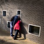 Elderly Couple Sharing Curiosity by Brick Wall Openings Elderly couple exploring brick wall openings in park with curiosity and companionship.