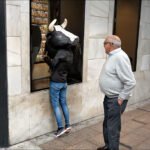 Playful Cow Costume Window Shopping on City Street Person in cow costume playfully window shopping on busy urban street with elderly man watching.