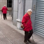 Elderly Couple in Red Coats Walking City Street Elderly couple in red coats walking on quiet urban street with shuttered storefront.