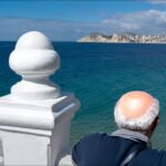 Elderly Man Gazing at Scenic Coastal City View Elderly man overlooking coastal city skyline with ocean view and mountains.