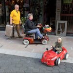 Family Outing With Child in Toy Car and Mobility Scooter Elderly couple with child in toy car enjoying family outing on urban shopping street.