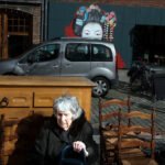 Elderly Woman by Street Mural in Urban Market Scene Elderly woman sitting by street mural with wooden chairs and urban market scene.