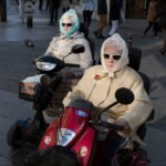 Stylish Elderly Women Riding Mobility Scooters in City Elderly women on mobility scooters wearing stylish coats and sunglasses in a busy city street.