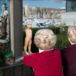 Elderly Women Viewing Saint Statue with Baby Doll Elderly women observing saint statue with baby doll at urban shrine.