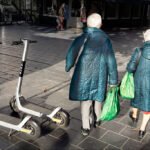 Elderly Women Strolling Past Scooters on City Street Two elderly women walking with scooters.