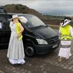 Elegant Women in White Dresses at Construction Site Elegant women in white dresses wearing safety vests at construction site with black van.