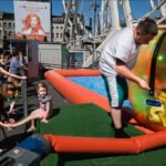 Summer Festival Fun With Kids in Water Walking Ball Kids playing in water walking ball at summer festival with Ferris wheel and crowd.