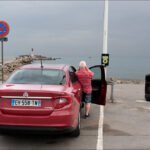 Red Fiat Tipo Parked by the Seaside Jetty Red Fiat Tipo parked by the seaside near jetty under cloudy sky.