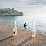 Fisherman on Pier With Beer Bottles by the Coast Fisherman on pier with beer bottles by scenic coastal shoreline at sunset.