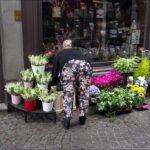 Woman Choosing Flowers at Charming Street Shop Woman shopping at colorful street flower shop with plants and bouquets on display.