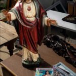 Jesus Statue Amid Magazines at Outdoor Market Jesus statue with sacred heart on rustic table surrounded by magazines at outdoor market.