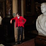 Man in Red Jacket Among Classical Marble Busts Man in red blazer posing with classical marble busts in historic museum interior.