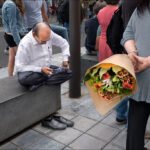 Elderly Man on Bench With Woman Holding Flowers Elderly man using smartphone on city bench while woman holds colorful flower bouquet nearby.