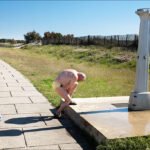 Elderly Man Rinsing at Beachside Outdoor Shower Elderly man rinsing at outdoor beach shower on sunny coastal promenade.
