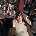 Sunlit Café Moments With Friends and Laughter Man shielding sun with menu at outdoor café while friends laugh and enjoy drinks.