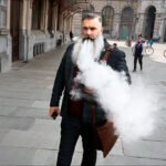 Stylish Bearded Man Vaping on Busy City Street Bearded man in plaid suit vaping on busy city street with smoke.