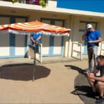 Men Relaxing Under Beach Umbrella at Motel Courtyard Men relaxing under striped beach umbrella outside motel on a sunny summer day.