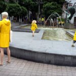 Mother and Children Playing by Fountain in Yellow Raincoats Mother and children in yellow raincoats playing near fountain in city park.