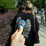 Colorful Painted Owl Rock at Outdoor Festival Hand holding painted owl rock at outdoor festival with people and greenery in background.