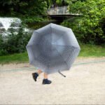 Stroll Through Park With Striped Umbrella and Fountain Person walking in green park with striped umbrella near fountain and garden path.