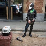 Man in Dog Mask Walking Ferret on City Street Man in dog mask walking pet ferret on city street in unique latex outfit.