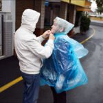 Caring Gesture on a Rainy Tropical Street Two people share rainy day companionship under palm trees with poncho and tropical street.